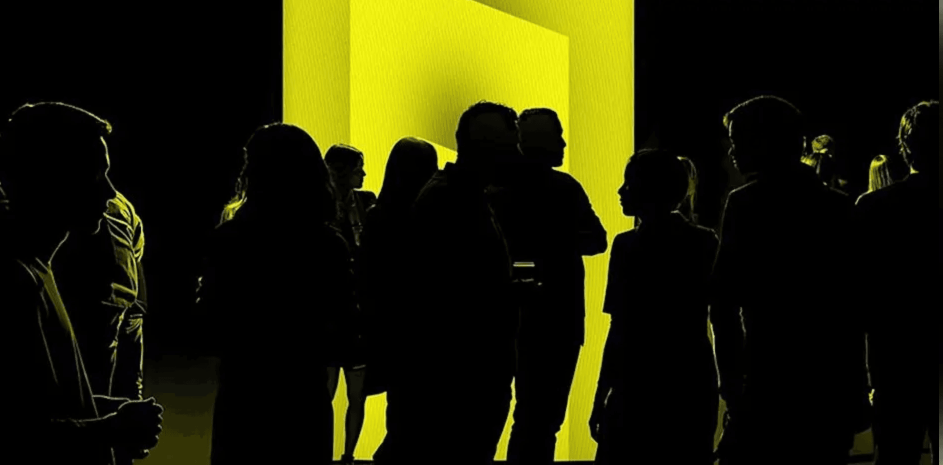 Silhouettes of people gathered in a dimly lit space, illuminated by a bright yellow rectangular glow in the background.