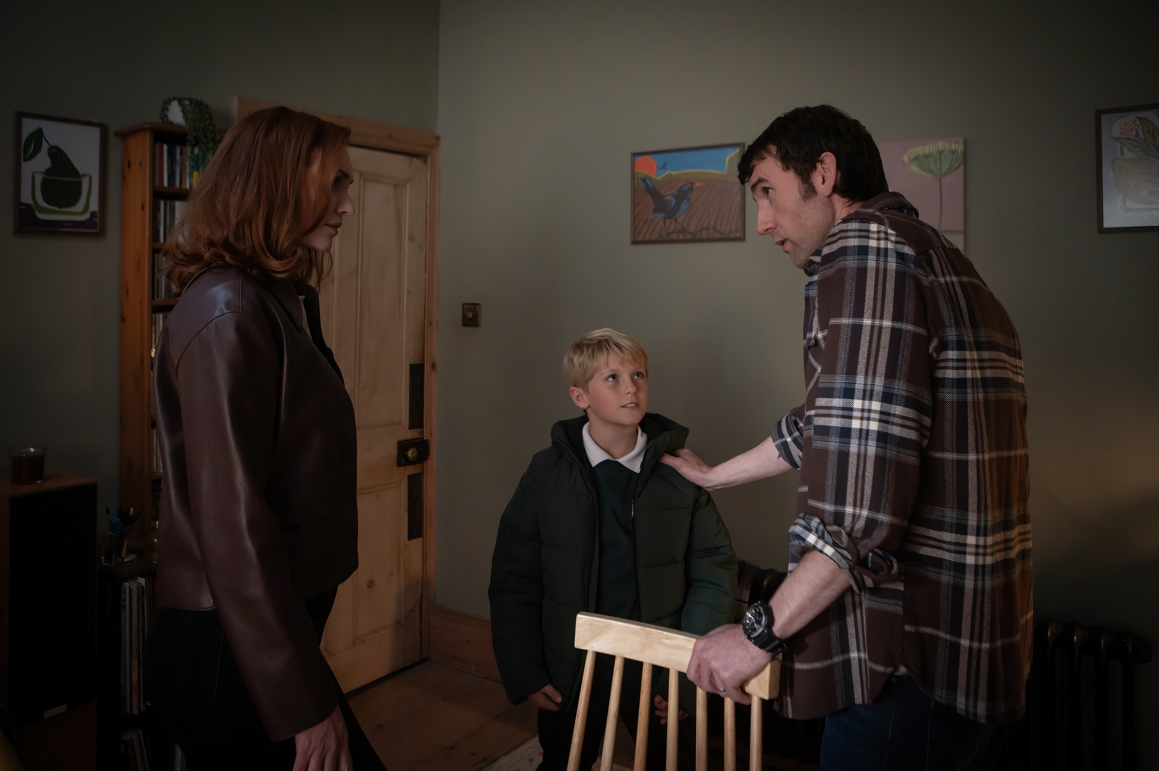 A family of three, an adult male, adult female, and a boy stand inside a room with the boy in the middle. The man has his hand on the boy's shoulder.